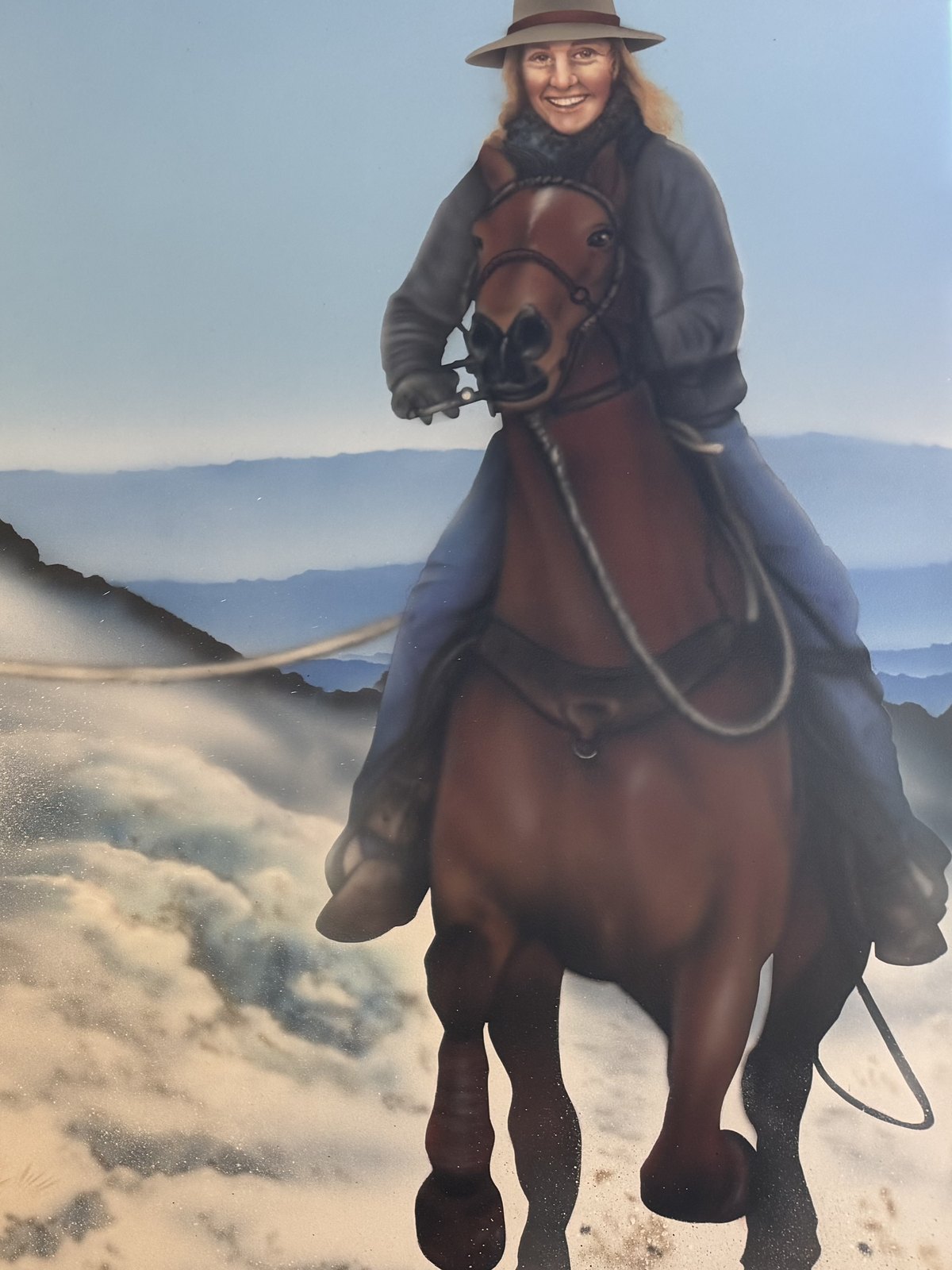 Leah riding a bay horse through snow with the blue ranges behind
