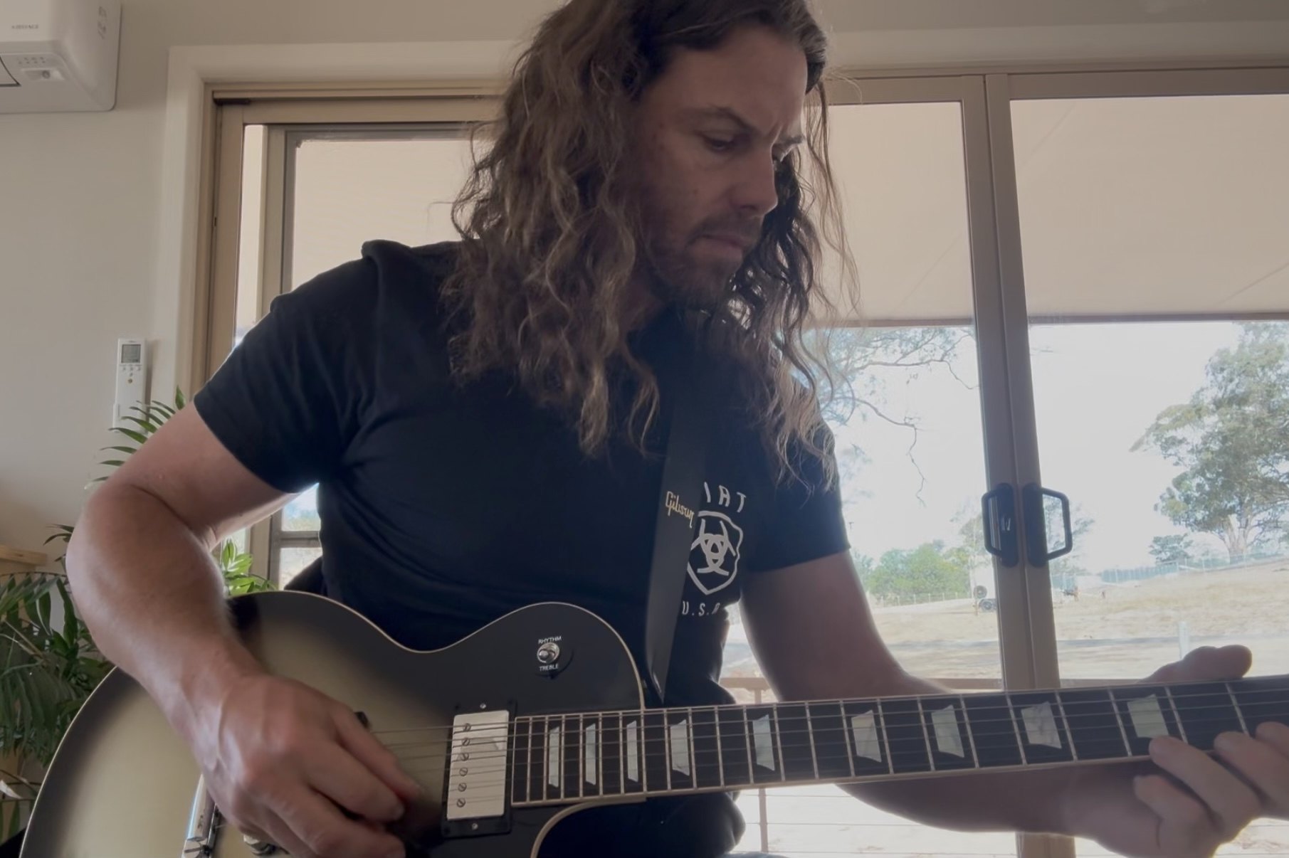 Mark Follett playing a Gibson Les Paul with the farm visible through the window