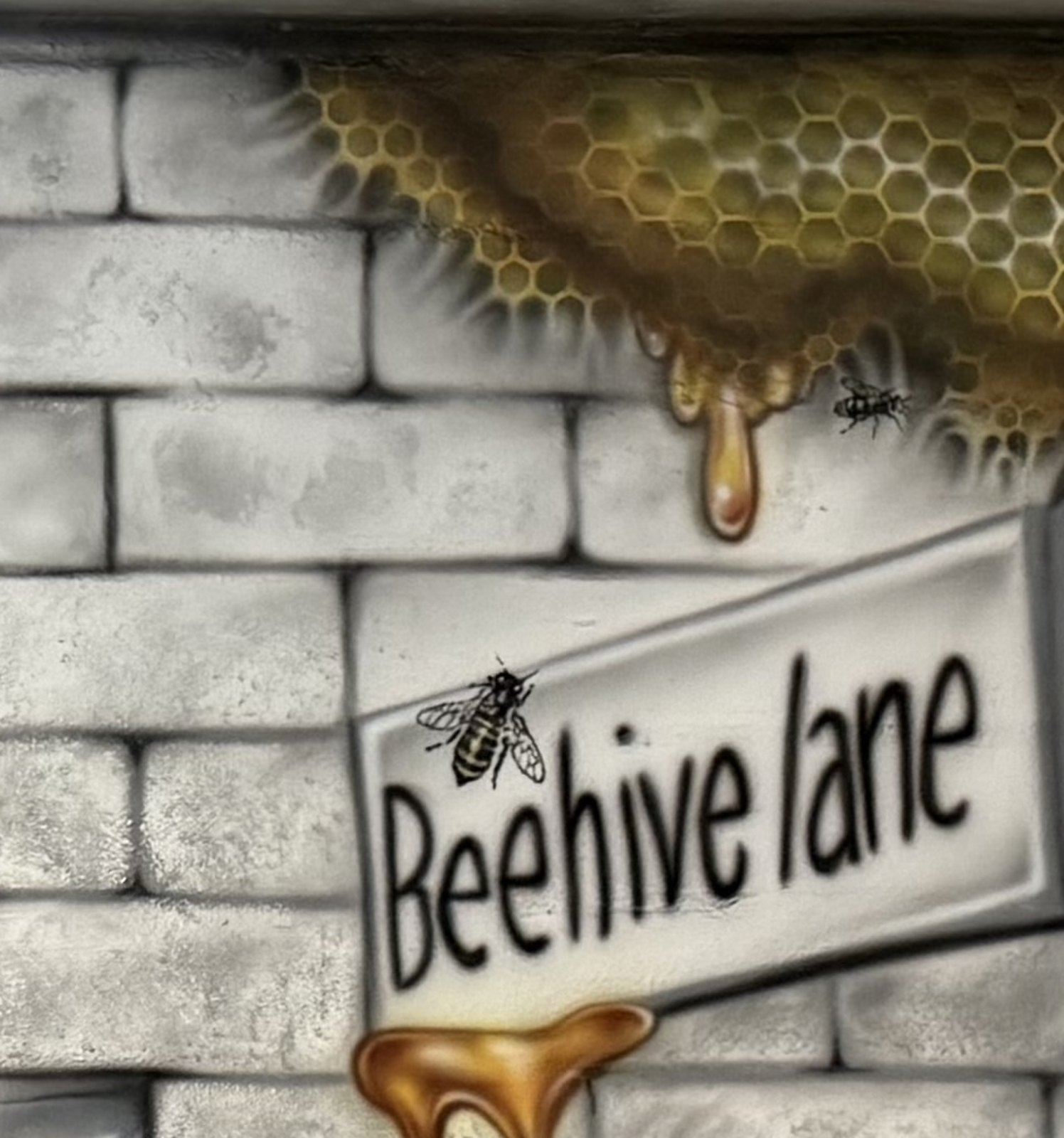 Honeycomb dripping over brickwork beside a Beehive Lane street sign